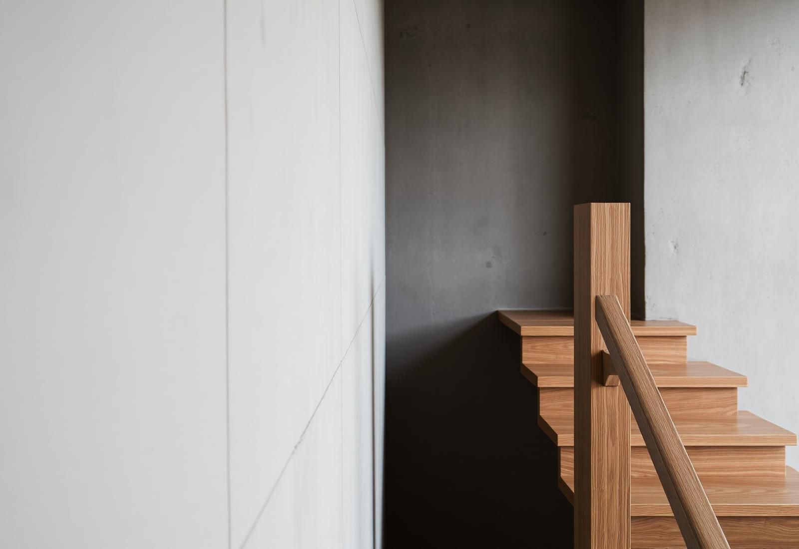 Detalle de la escalera de roble contra el muro de hormigón